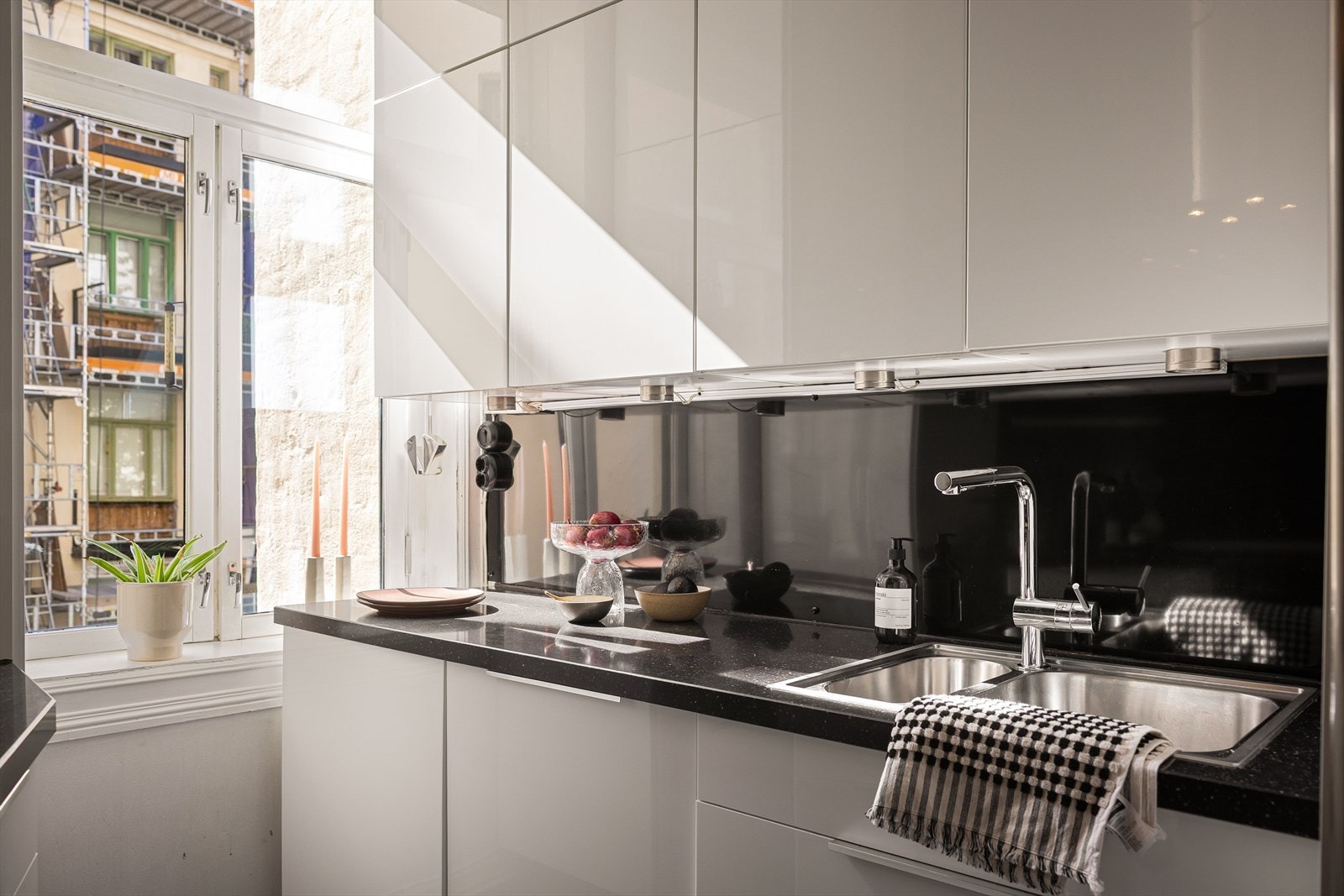 Lys innredning med hvite, glatte høyglans fronter, plater på veggen over kjøkkenbenken og benkeplate i stein. Galleribilde