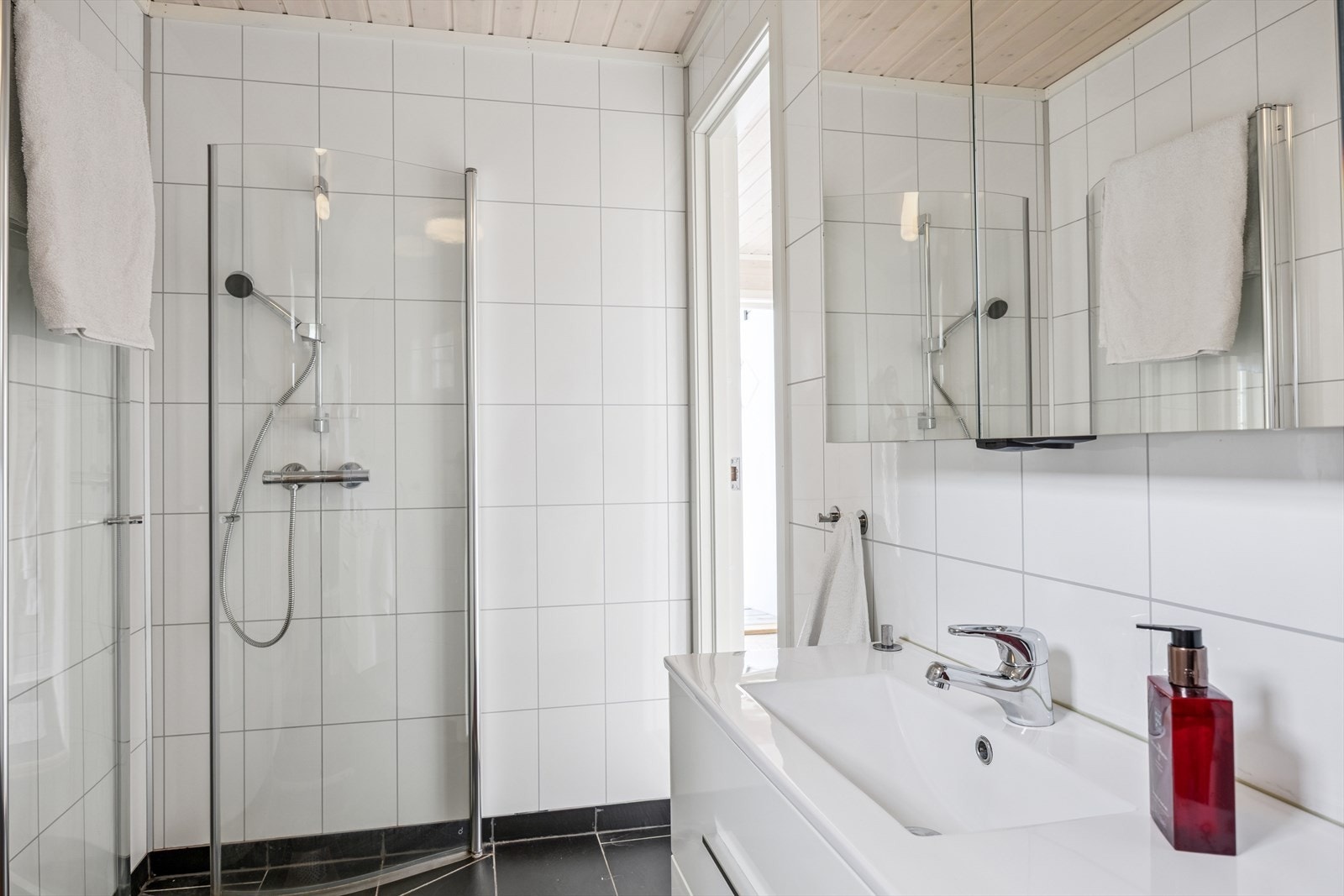 Badet har fliser på gulv og baderomsplater på vegg. Rommet er innredet med baderomsinnredning, toalett og dusjløsning. Galleribilde