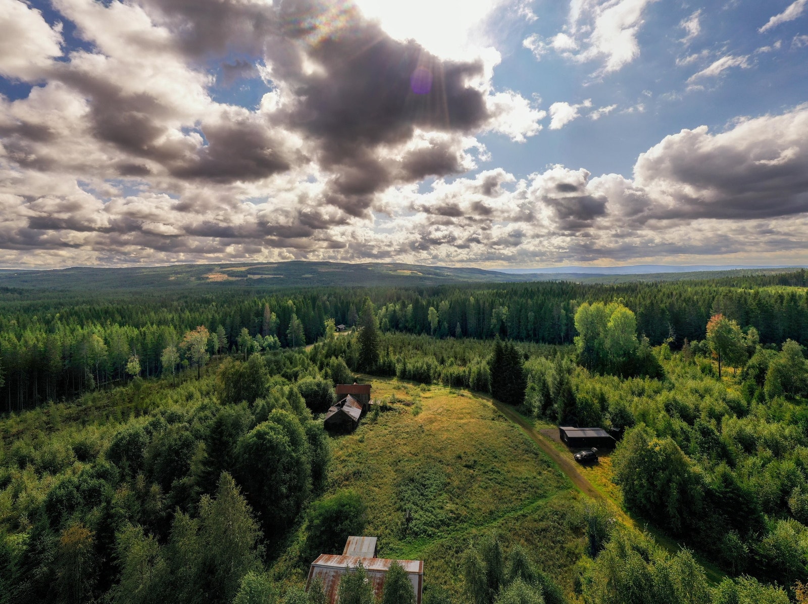 Oversiktsbilde som viser tomten med hytta, en eldre låve og en brakke. Galleribilde