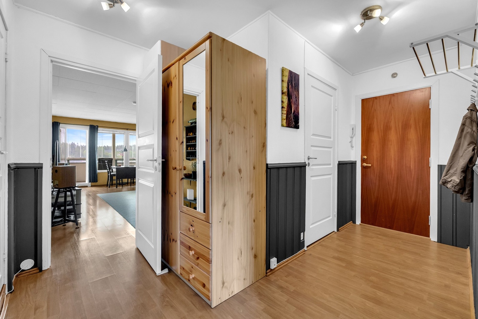 Når du trer inn i leiligheten, møtes du av en lys og romslig entré med hvitmalte vegger og elegant mørk brystning. Galleribilde