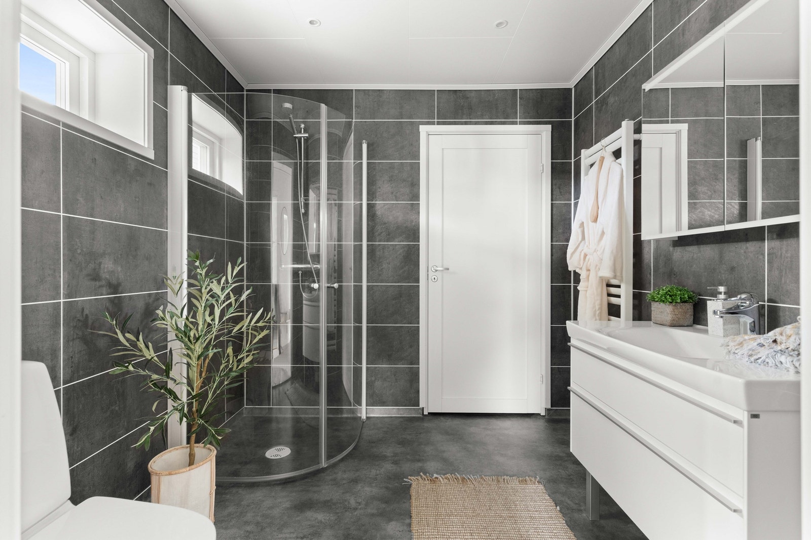 Stilrent bad med mørke fliser, hvit innredning og praktiske løsninger. Galleribilde