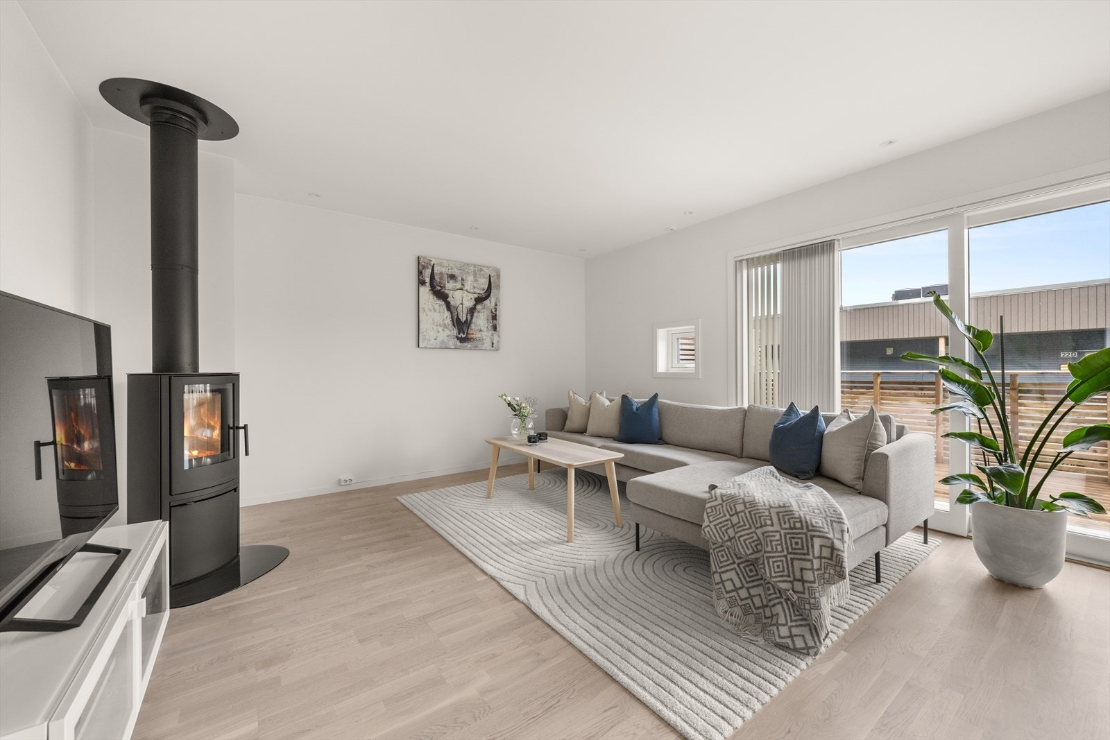 Lekker og stilren peisovn med stålpipe i taket er som prikken over i-en. Det er montert lameller og plissegardiner foran vindusflatene. Stuen har ellers god plass til møblering med stor sofagruppe og tilbehør Galleribilde
