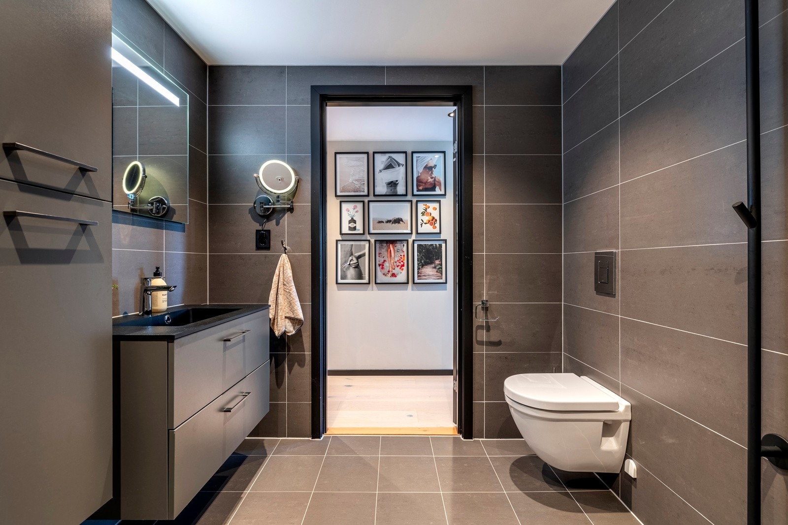 Badet ved entréen er stilfullt innredet med servantinnredning, speil med lys på vegg over servant, et sminkespeil med lys, vegghengt toalett og dusjhjørne med svingbare glassdører. Galleribilde