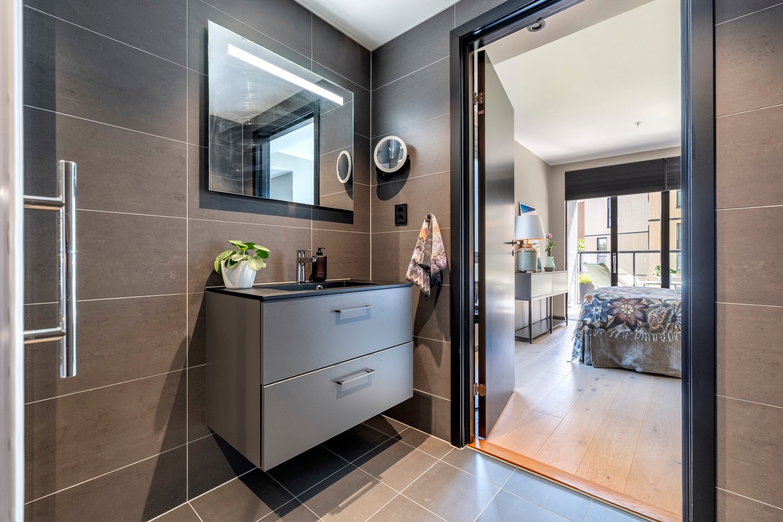 Badet har et stilrent utrykk med vegg- og gulvfliser i mørkegrå toner, varmekabler, innfelt downlights og balansert ventilasjon. Galleribilde
