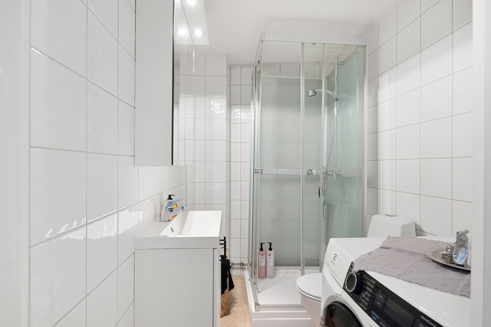 Badet er innredet med gulvstående toalett, dusjkabinett samt servant med skap, speil og belysning. Galleribilde