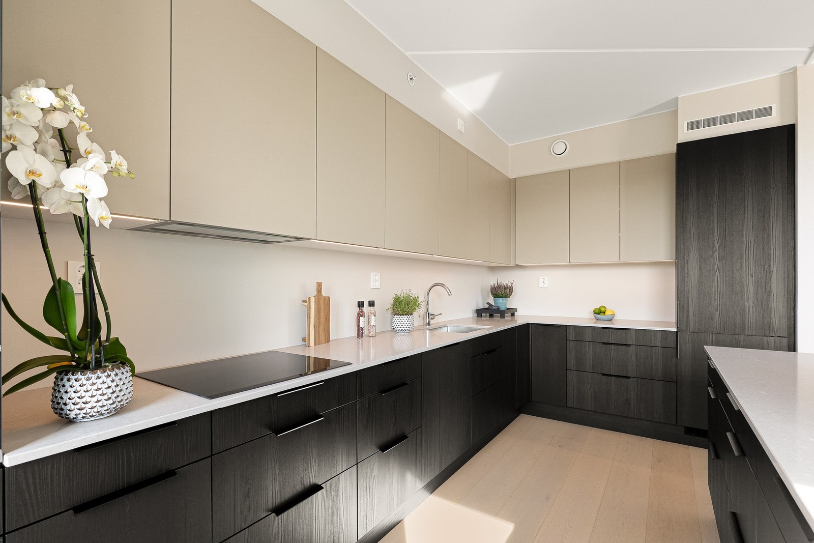 Innredningen kombinerer mørke, eikestrukturerte fronter på benkeskap og høyskap med varme beige overskap. Galleribilde