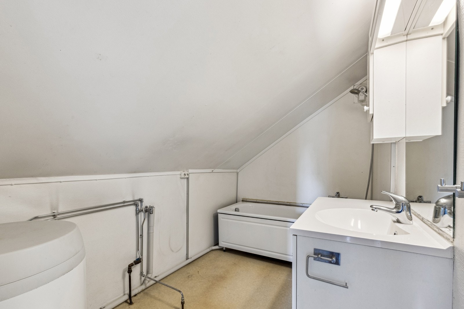 Badet er innredet med dusj i badekar, et toalett, hvit servantinnredning og en varmtvannsbereder fra 2014. Galleribilde