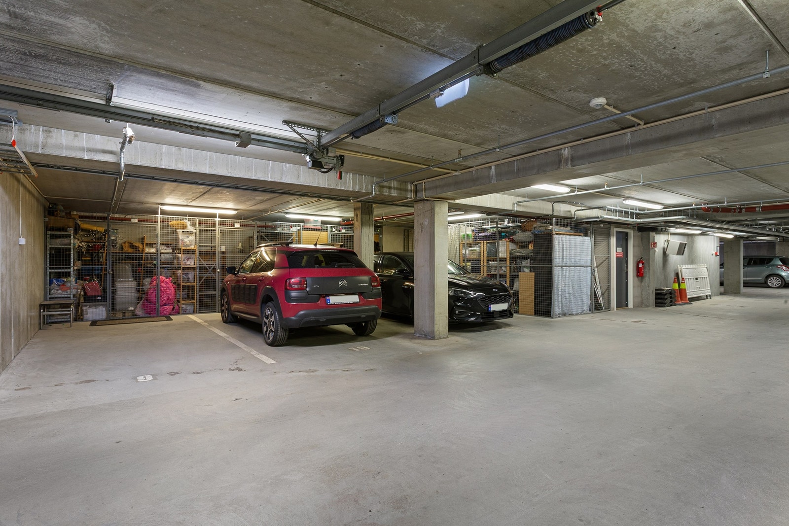 Leiligheten har to parkeringsplasser i felles garasjekjeller. Det er de to til venstre på på bildet som følger. Bod rett i front av rød bil på bildet hører til denne leiligheten. Bod er 6 kvm. Galleribilde