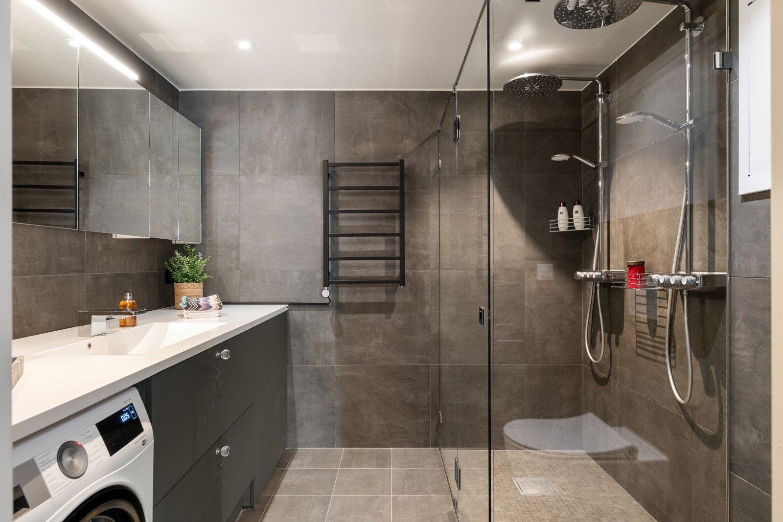 Badet, tilknyttet hovedsoverommet, har fliser valgt i tilvalgsprosess, spesialtilpasset innredning fra Bekkestua Kjøkkenstudio (2020/2021), speilskap fra Sigdal og benkeplate i corian med helstøpt servant Galleribilde