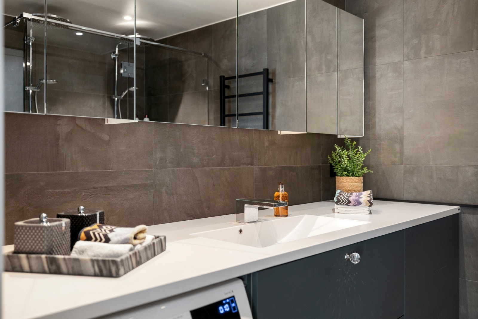 Det er plass til både vaskemaskin og tørketrommel. Dusjnisjen er utvidet og utstyrt med spesialtilpassede dusjvegger fra Iconic Nordic Rooms, samt både regnfallsdusj og håndholdt dusj. Elektrisk håndkletørker er også på plass Galleribilde