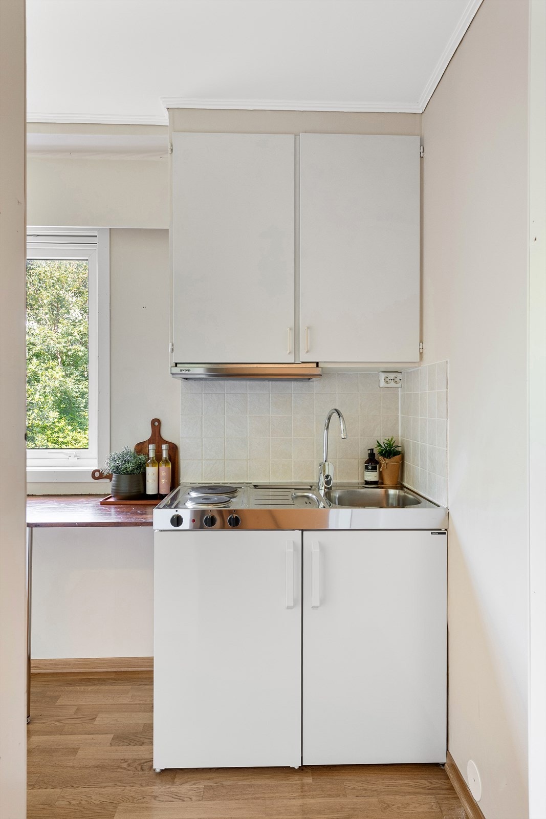 Enkelt minikjøkken med integrert kjøleskap og to kokeplater. Det er i tillegg montert eldre overskap med innfelt ventilator Galleribilde