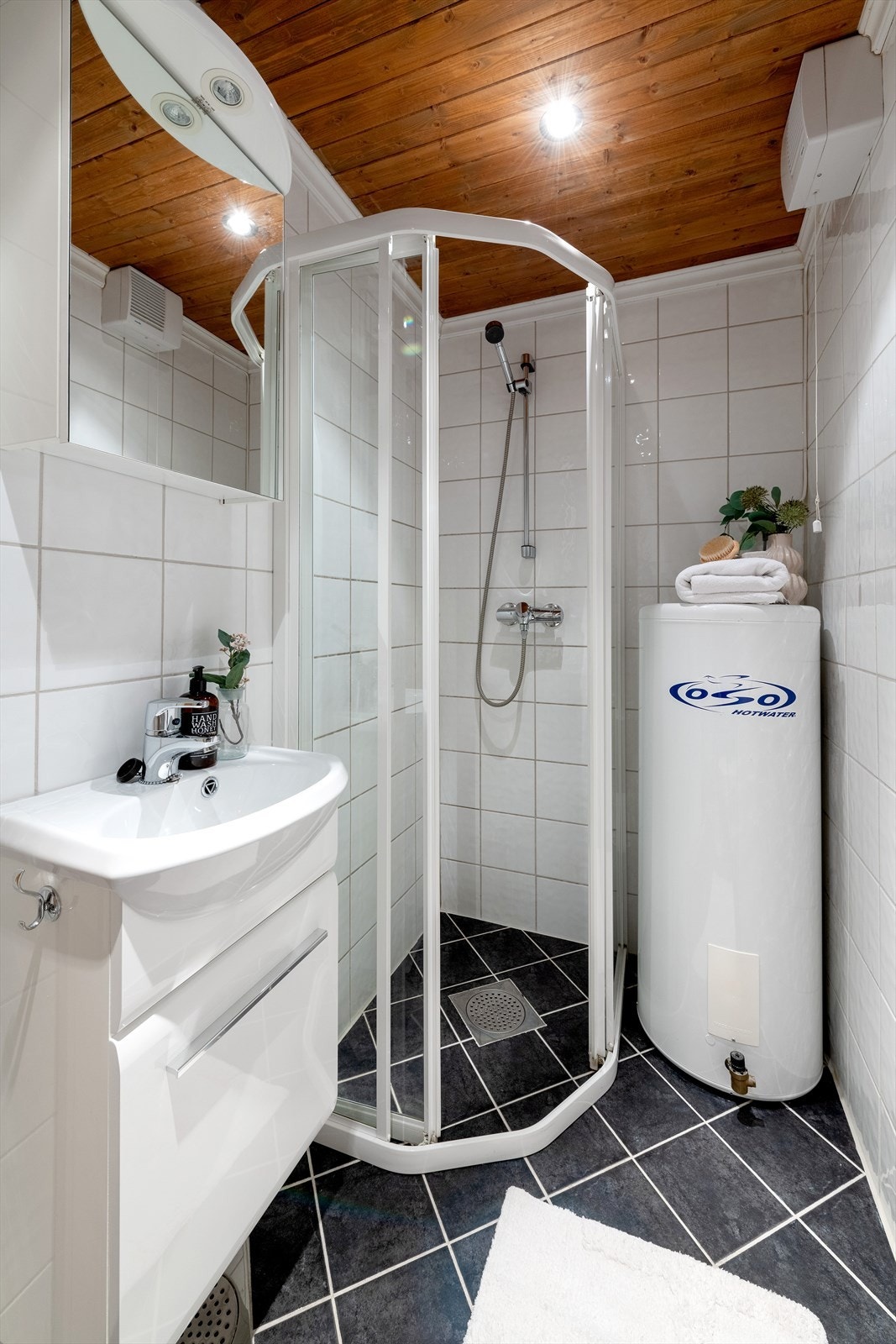 Flislagt bad med dusjhjørne og innredning. Varmtvannsbereder plassert i hjørne Galleribilde