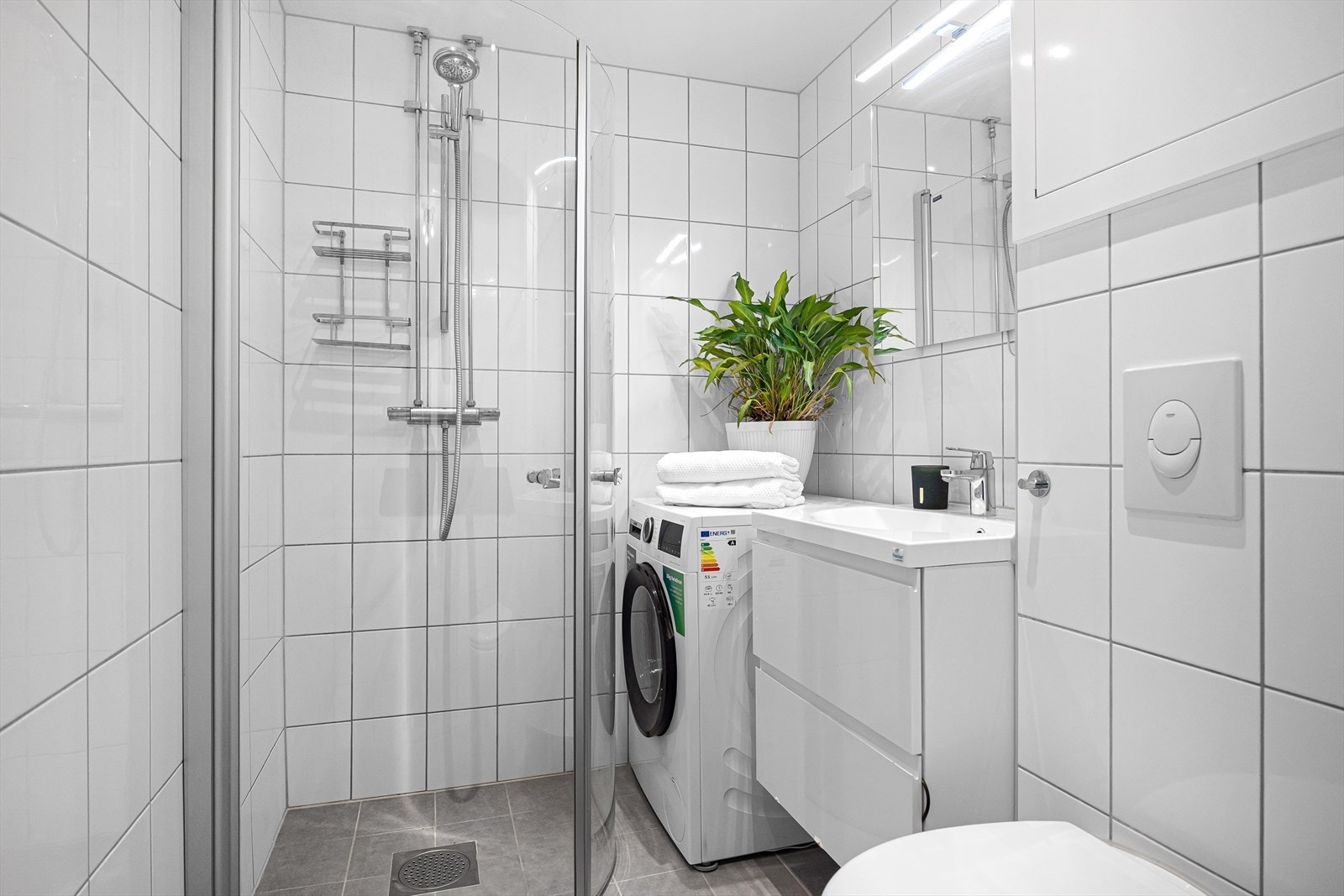 Badet har praktisk dusjhjørne med innfellbare dusjdører, opplegg for vaskemaskin, servant med innredning, toalett og varmekabler i gulv Galleribilde