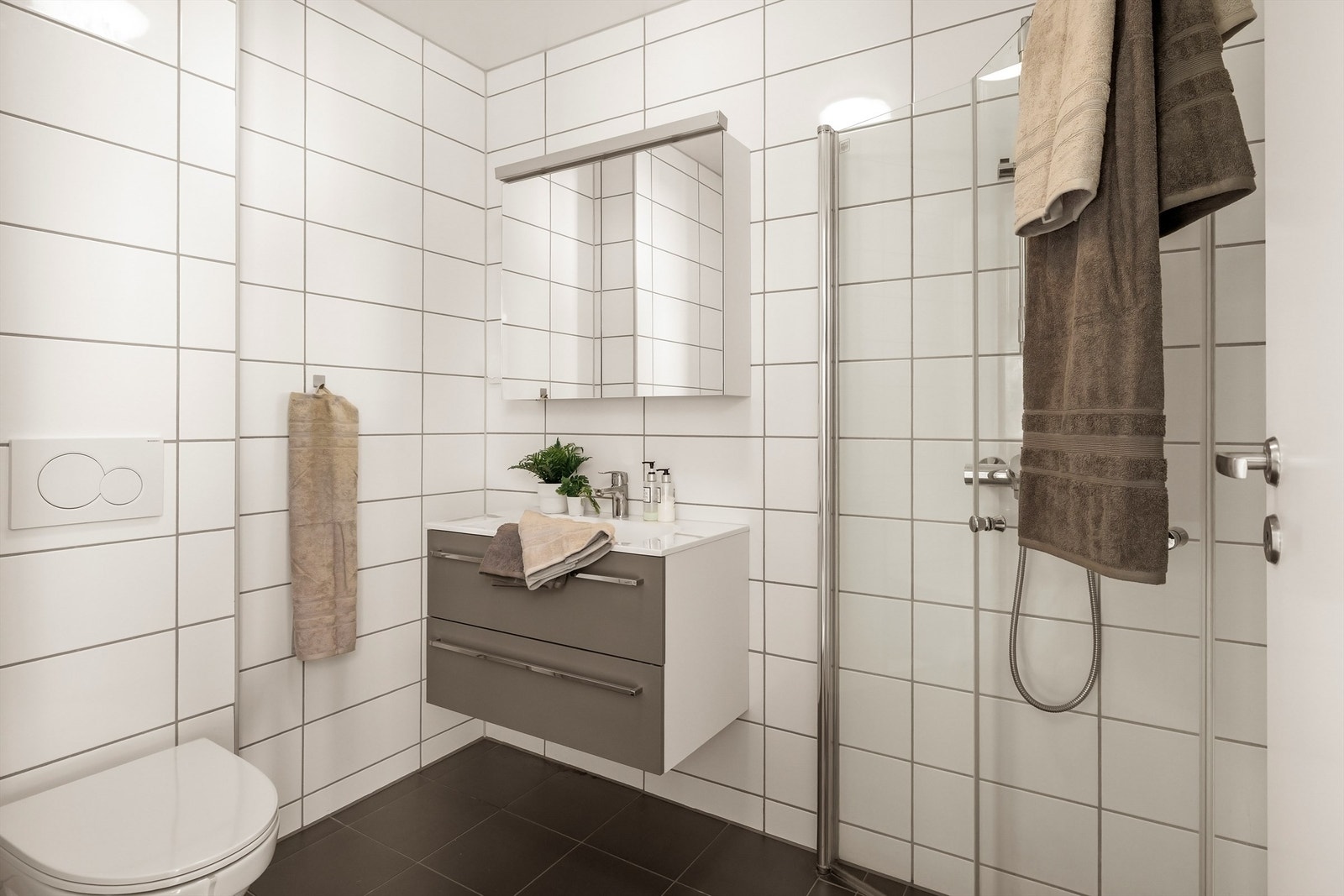 Helfliset lekkert bad/wc med tidløse fliser på gulv og vegger. Vegghengt toalett. Galleribilde