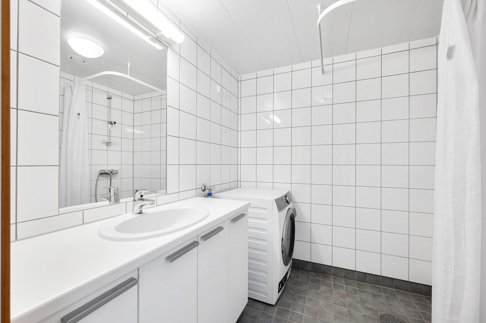 Flislagt bad med dusj og opplegg for vaskemaskin. Galleribilde