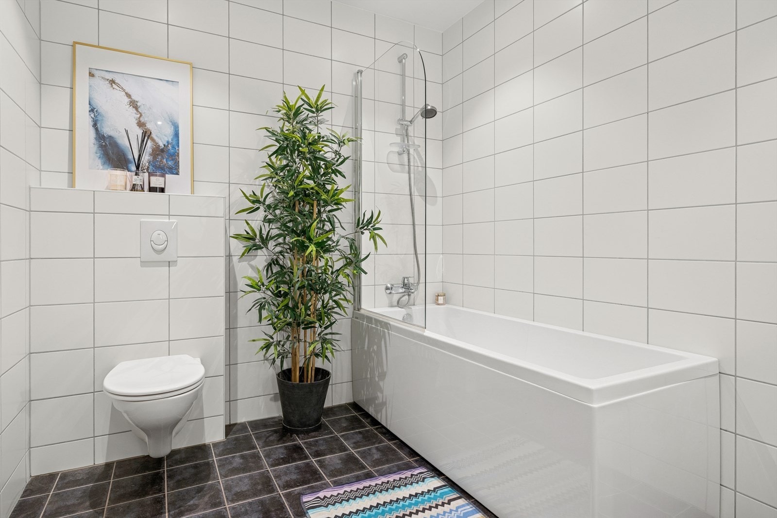 Våtrommet er utstyrt med innredning med nedfelt servant, veggmontert toalett, høyskap og badekar med sprutvegg. Galleribilde