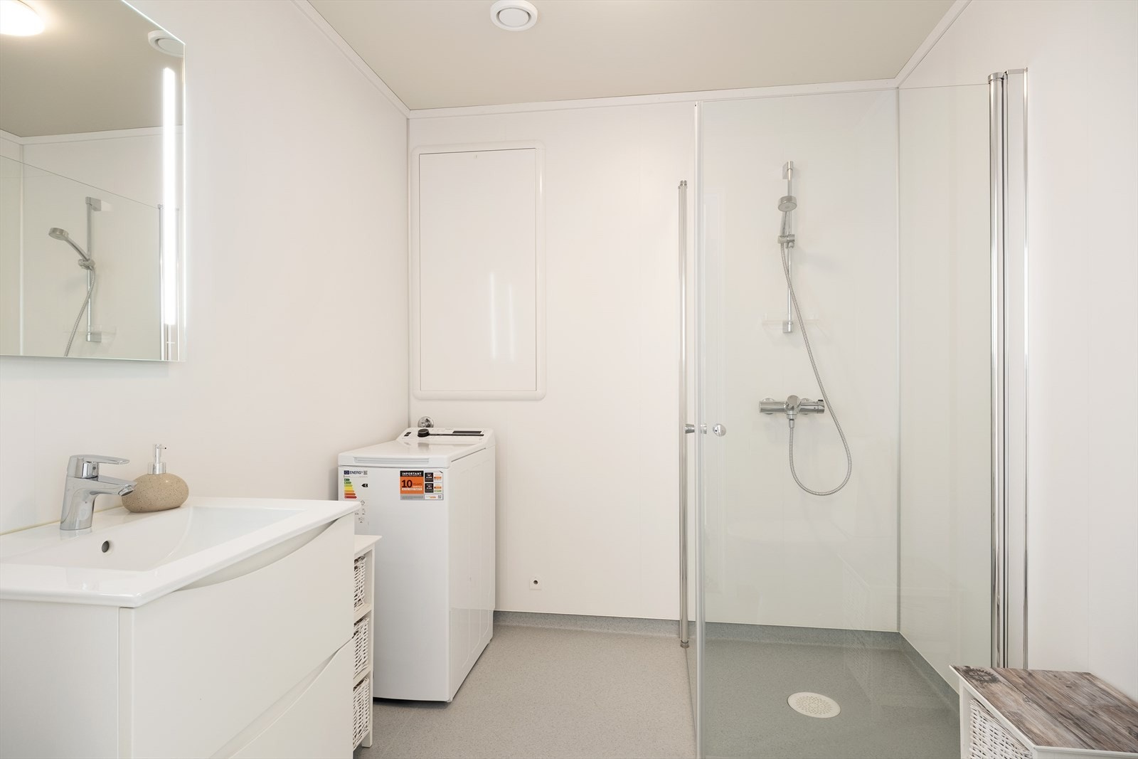 Kombinert bad/vaskerom med belegg på golv, baderomspanel på veggar og måla himling. Innreiing består av toalett, nedfelt servant med underskuffer, opplegg for vaskemaskin og dusjhjørne med glasdører. Galleribilde