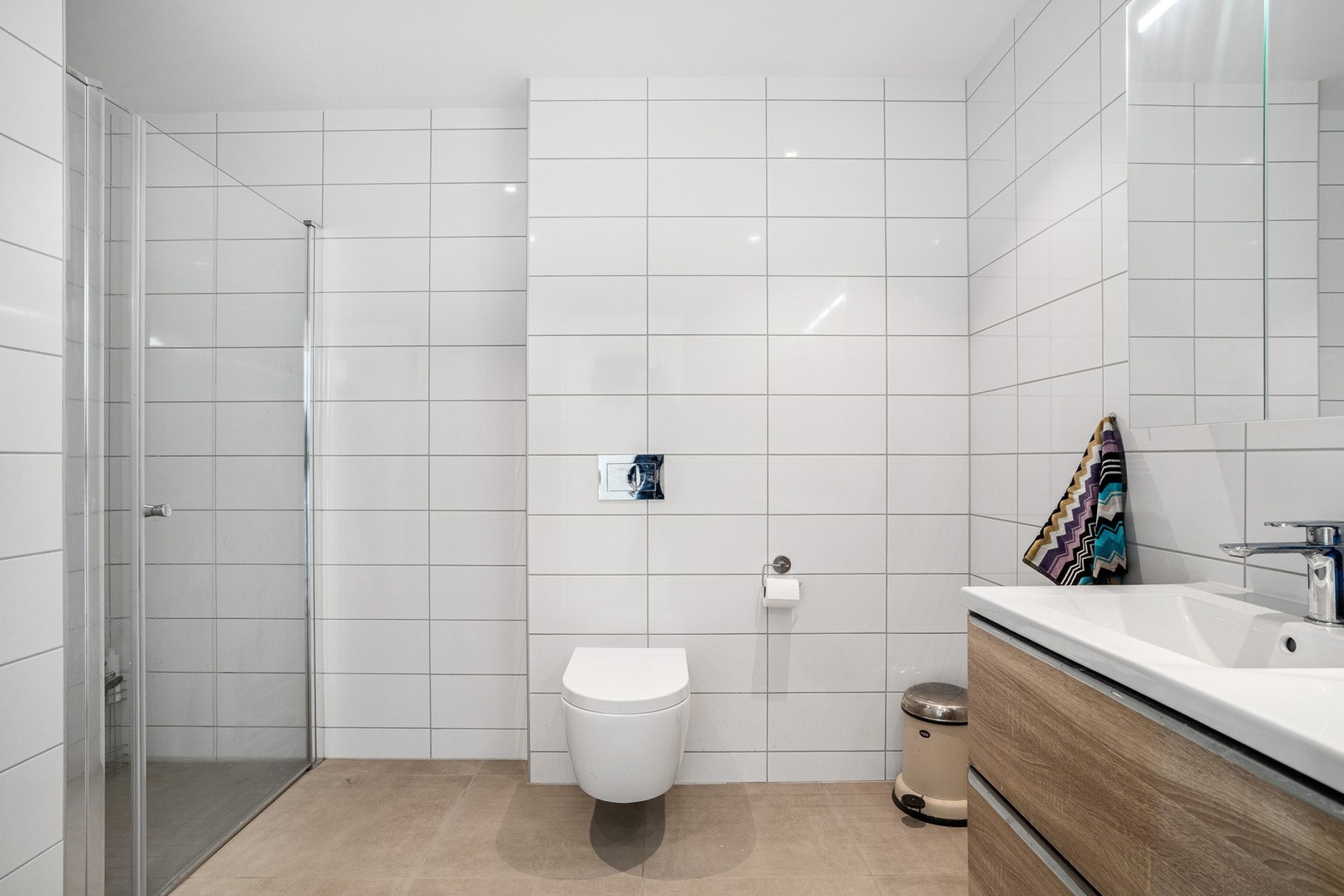 Badet inneholder dusj med innfellbar glassdør, vegghengt toalett, servant og speil. Galleribilde