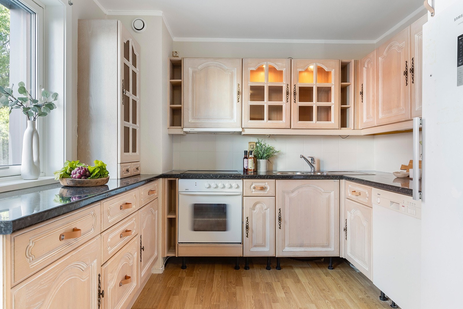 Kjøkkeninnredning med profilerte finerte skapfronter, laminert benkeplate med fliser på bakvegg, 1 1/2 oppvaskkum med benkebeslag, ventilator og innfelte hvitevarer som koketopp, stekeovn, frittstående oppvaskmaskin, kjøl/- fryseskap. Galleribilde