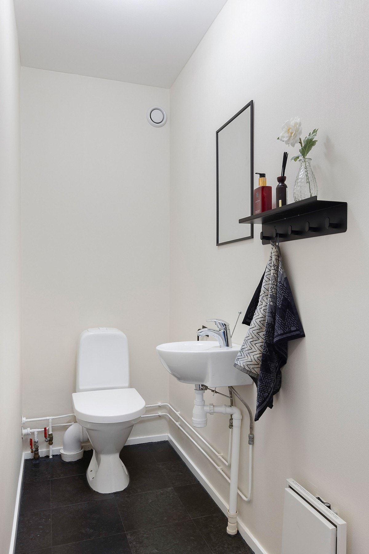 Vegg i vegg med badet, er det et praktisk toalettrom. Rommet er innredet med servant, speil og gulvmontert klosett. Det er lagt ny vinylfliser på gulv. Galleribilde