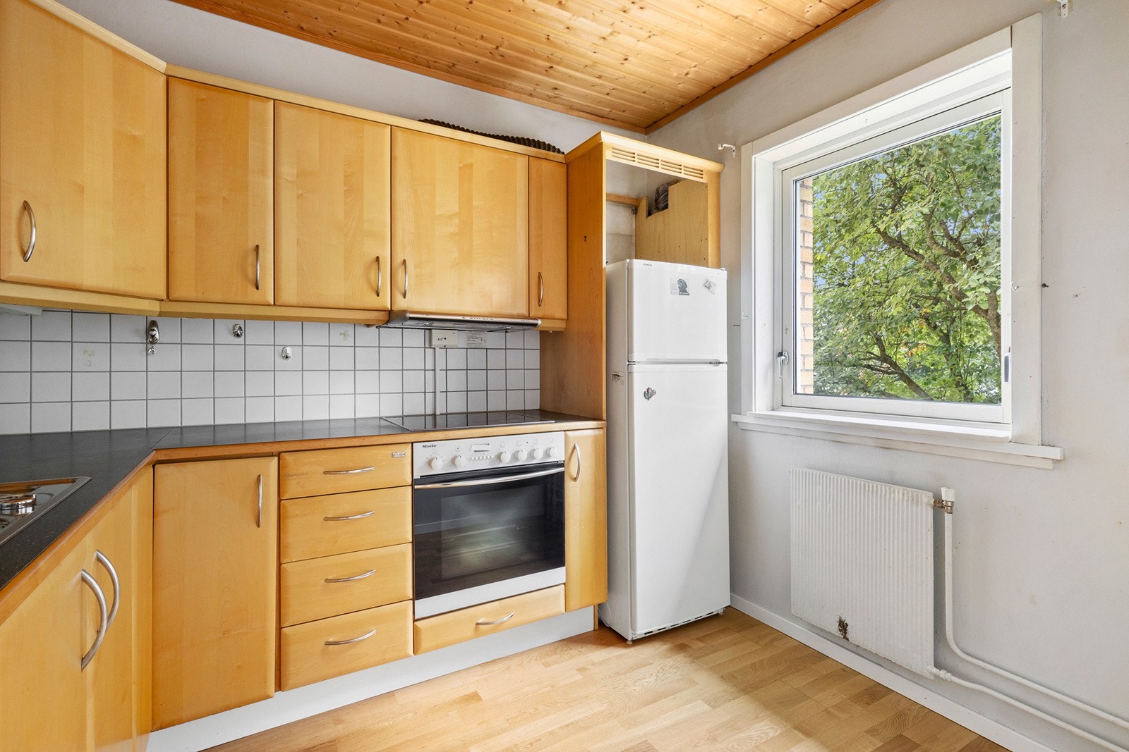 Kjøkken med finerte fronter, vitrinedører, laminat benkeplate og flisfelt over benk. Galleribilde