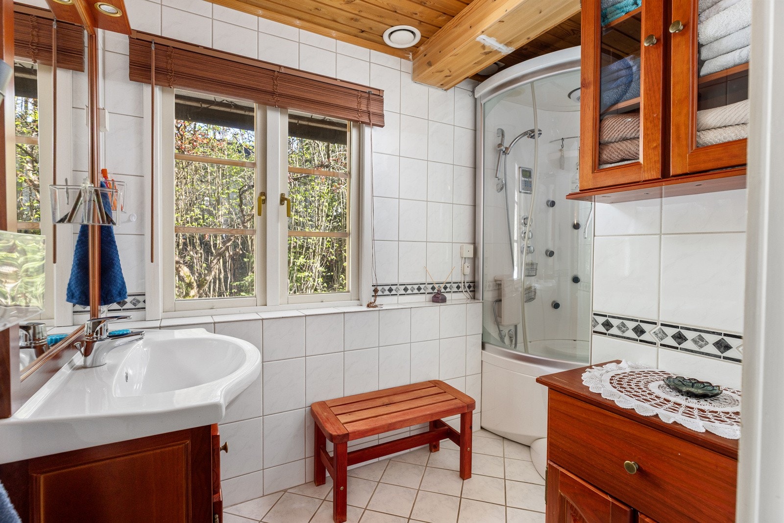 Badet i 1. etasje har flislagte gulv og vegger i klassisk utførelse. Rommet er innredet med dusjkabinett, servant og et praktisk benkeskap med profilerte fronter. Galleribilde