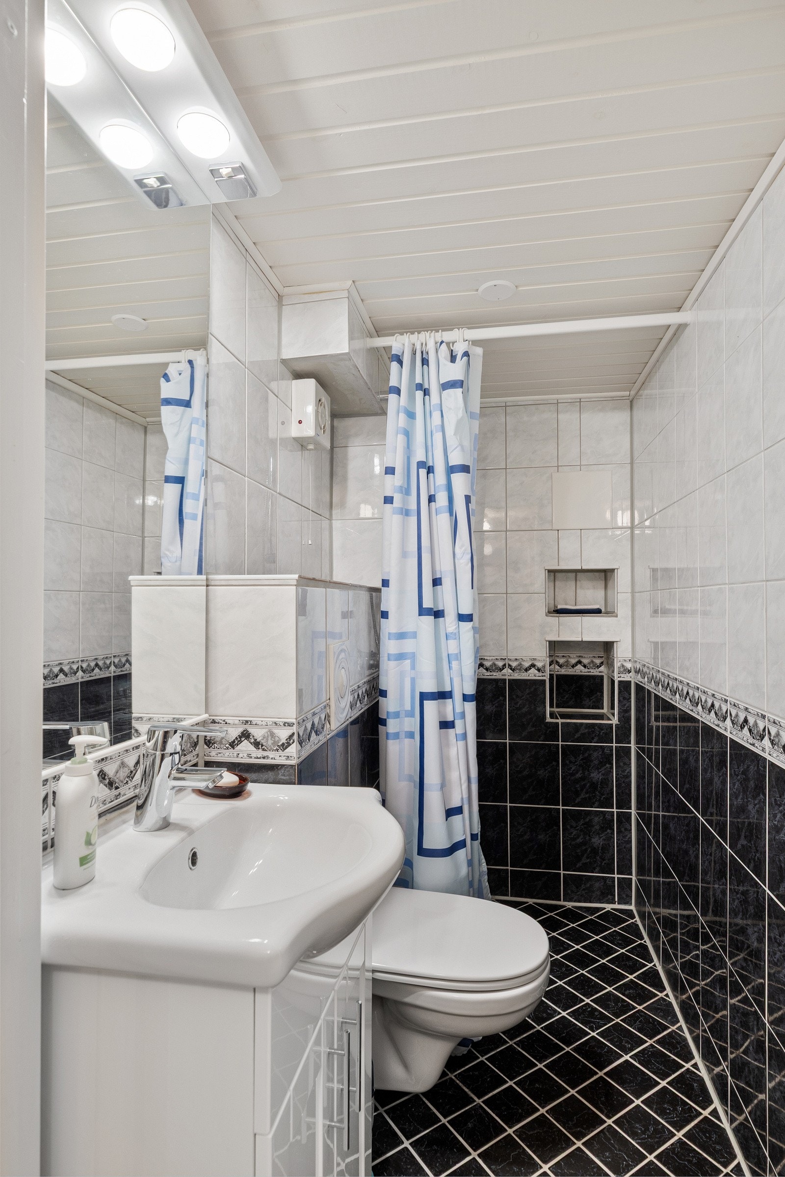 Badet i kjelleren er av eldre dato, med gulv og vegger som er flislagte. Rommet er utstyrt med dusj på gulv, servant og veggfestet toalett. Galleribilde