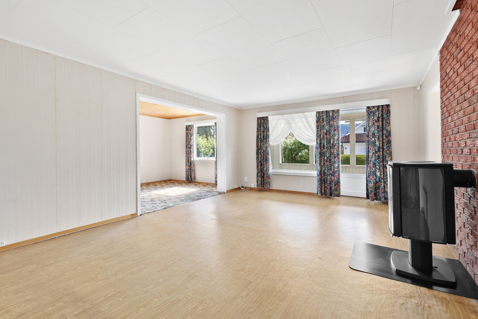 Lys og åpen stue med belegg på gulv, tapet på vegger og takplater i himling Galleribilde