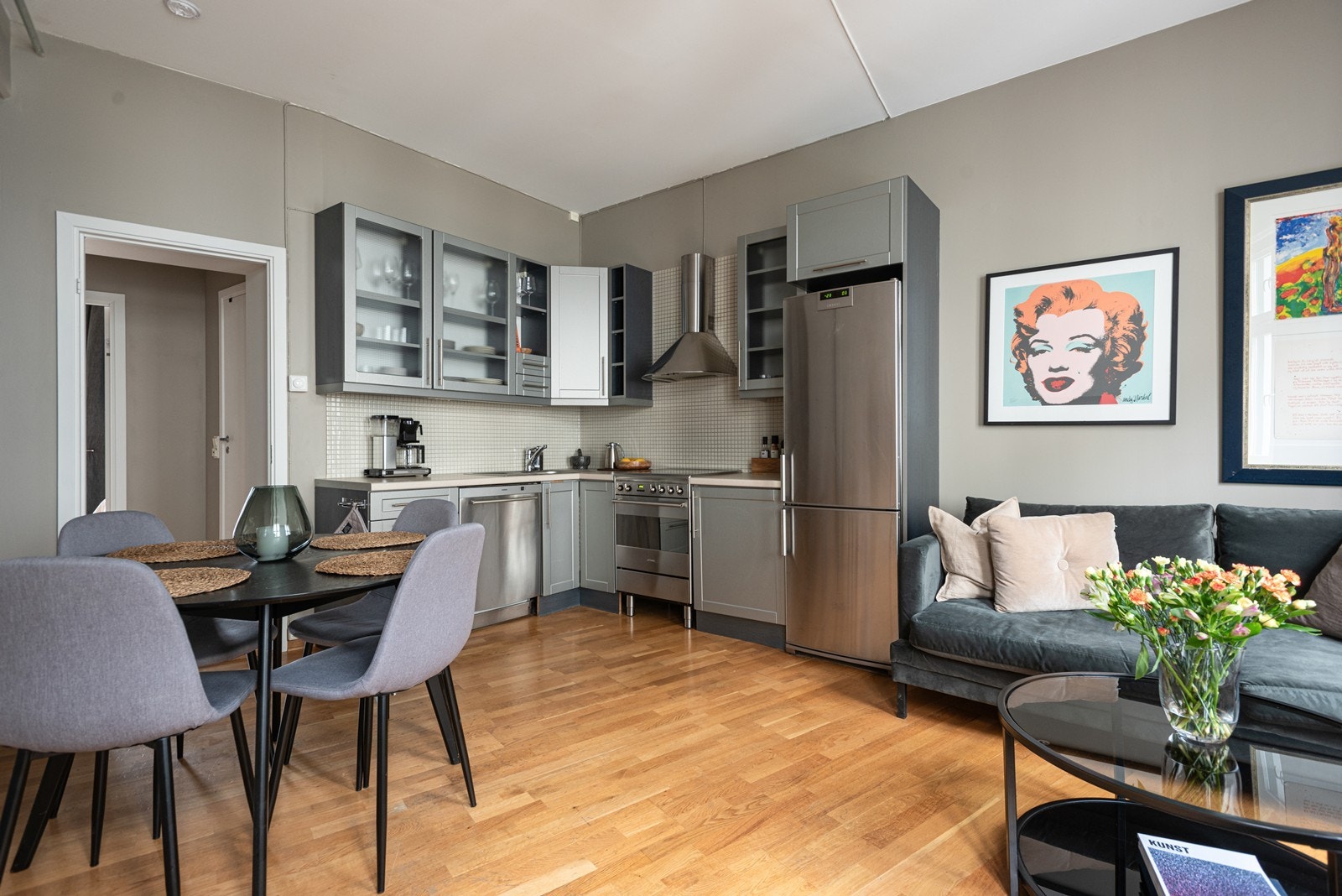 Flott kjøkken med slette fronter og benkeplate med nedfelt koketopp og oppvaskkum av stål. Stekeovn (Smeg komfyr), kjøleskap og oppvaskmaskin er frittstående Galleribilde