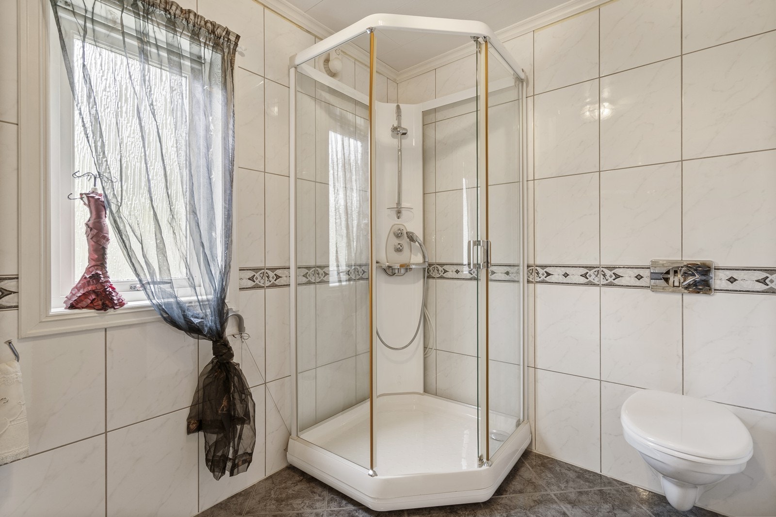 Badet inneholder vegghengt toalett, dusjkabinett og vask i stor seksjon med oppbevaring. Galleribilde