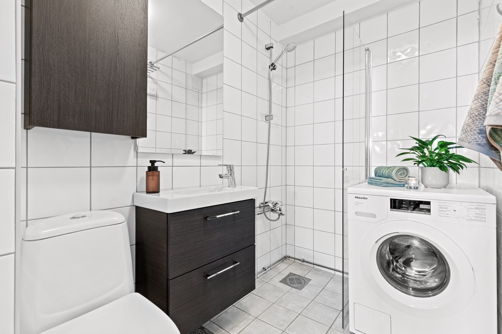 Badet har skap med glatte fronter og speil over servant. Videre har badet klosett, dusj og opplegg for vaskemaskin. Galleribilde