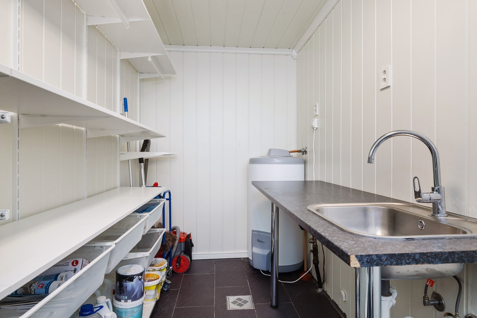 Man har også et vaskerom med fliser og varmekabler i gulv, og panel på vegger og i tak. Det er utstyrt med veggehengt garderobesystem, benkeplate med utslagsvask og opplegg for vaskemaskin. Galleribilde