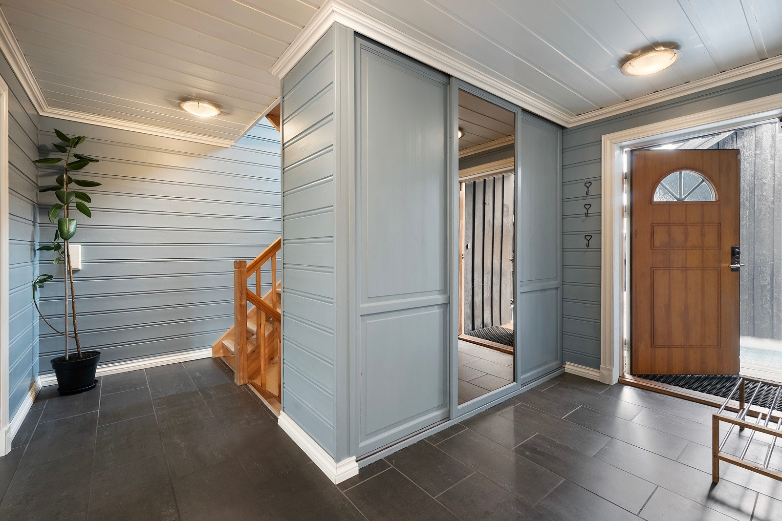 Her kommer du inn i en åpen og romslig entré med flislagt gulv og praktisk skyvedørsgarderobe Galleribilde