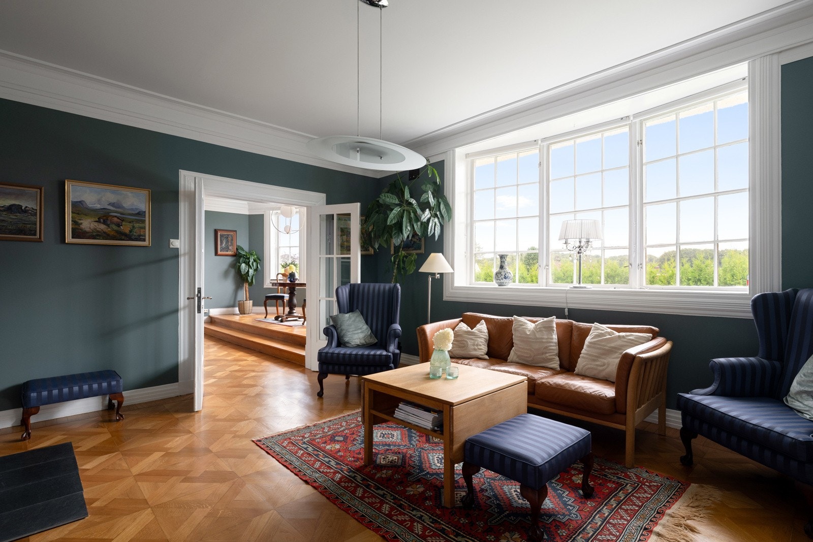 Lekre og store sprossevinduer som er med på å skape den gjennomførte stilen. Her finner man et stort, buet trefagsvindu. Gulvet er hevet ved vinduet, og i motsatt ende er det åpen forbindelse til hallen. Galleribilde