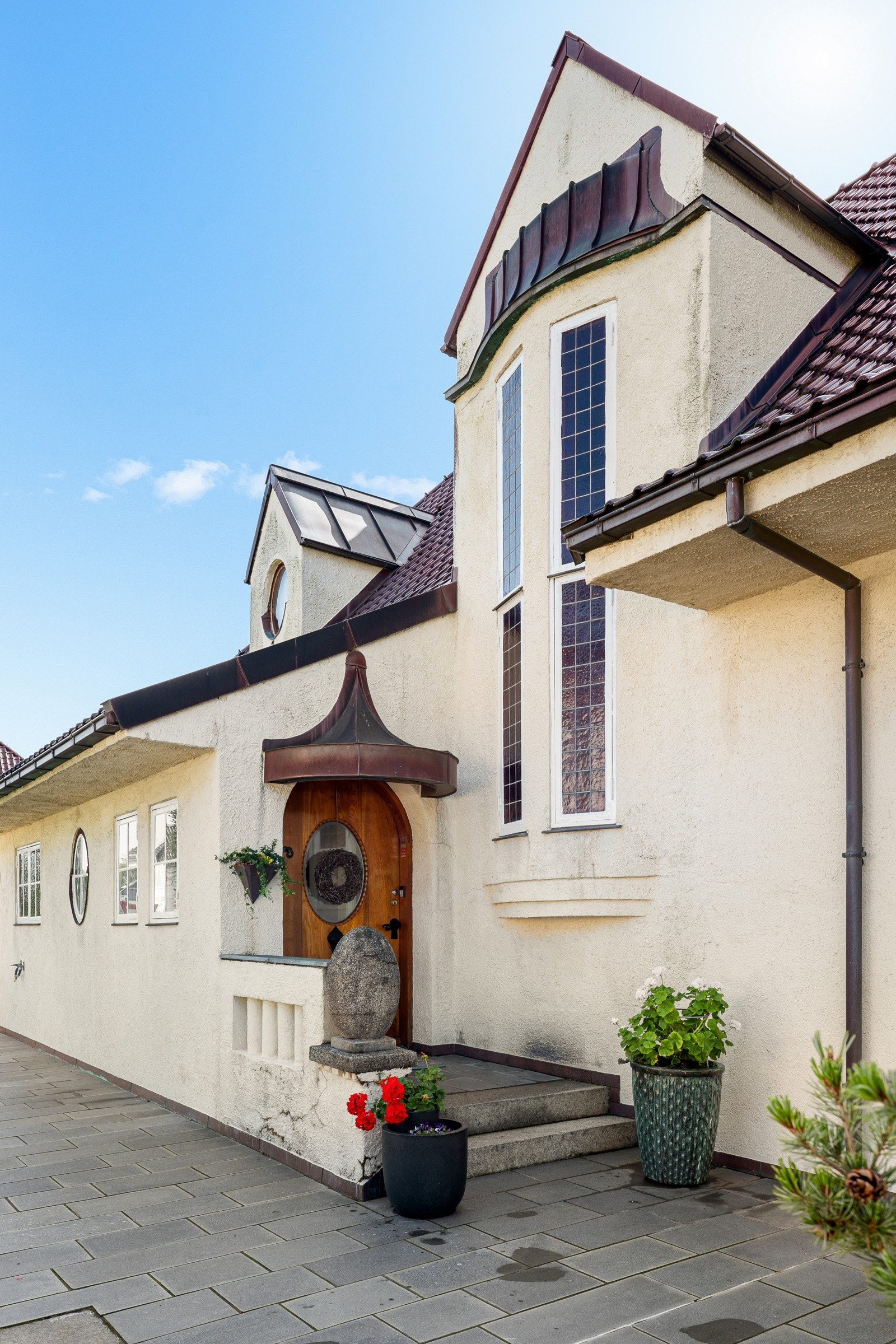 Nydelig inngangsdør i teak med dekorbeslag. Over døren er det et sjarmerende og særegent kobbertak formet som en halvmåne. Galleribilde