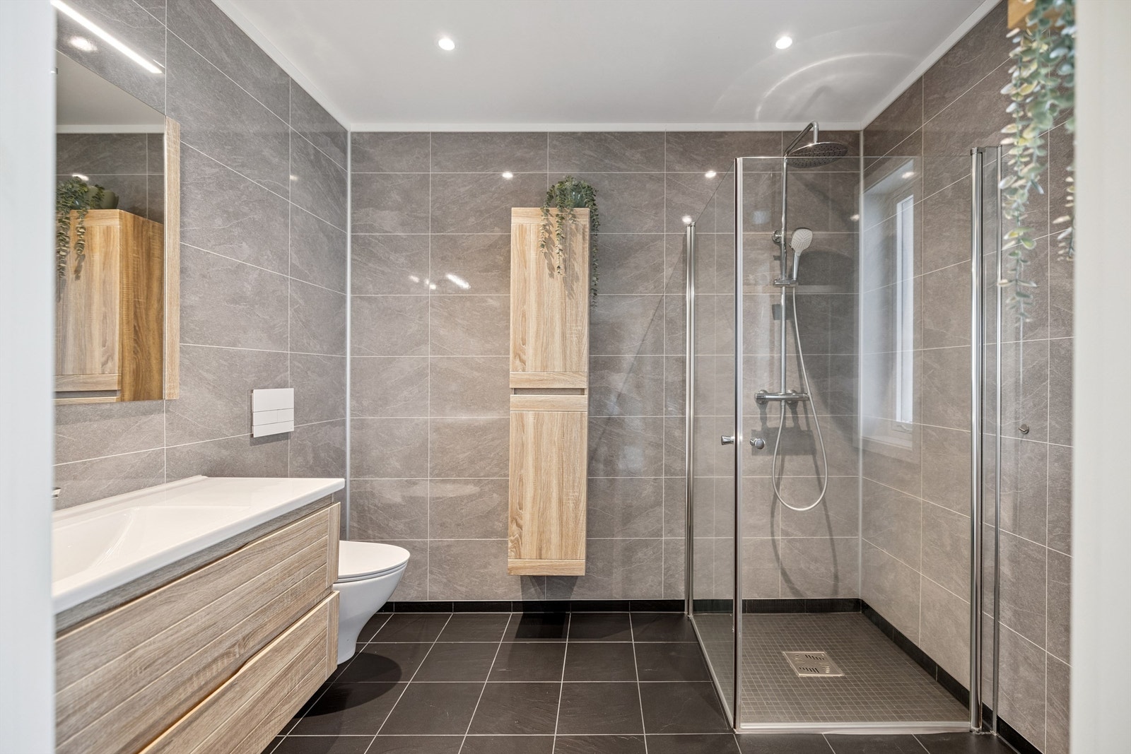 Pent bad utstyrt med dusjhjørne med glassdører og vegghengt toalett. Galleribilde