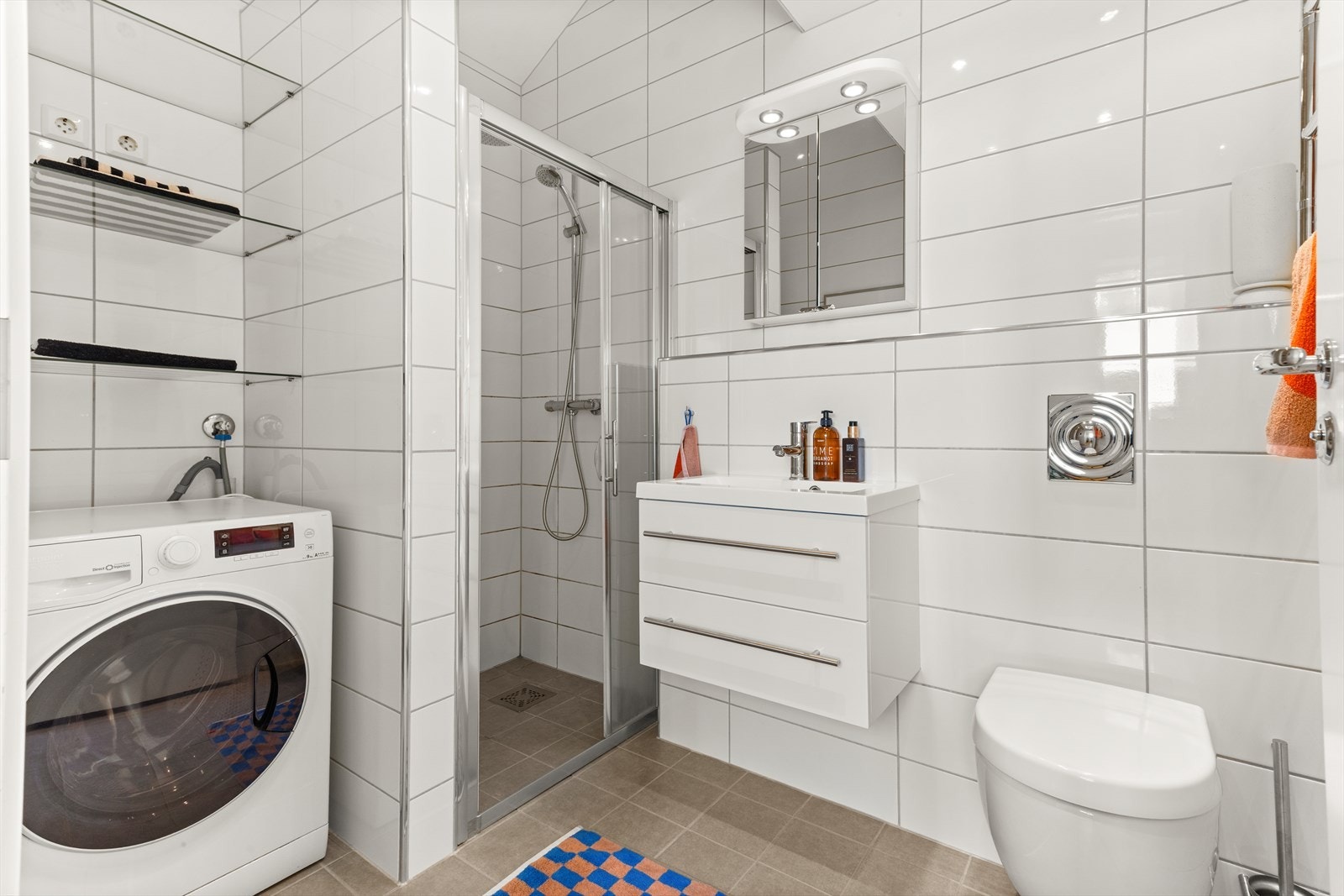 Badet er innredet med nedfelt servant med underskap, speil, toalett, håndkletørker og dusjhjørne med skyvbare glassdører Galleribilde