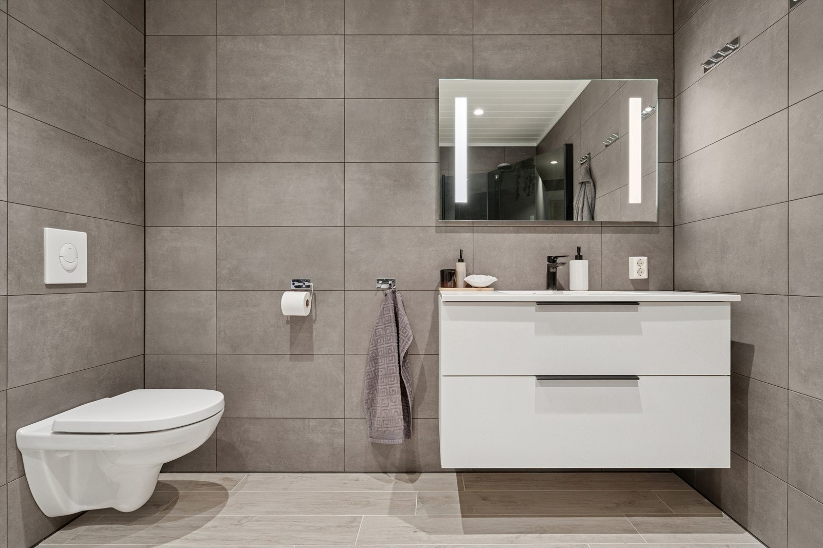 Badet er utstyrt med dusjhjørne, vegghengt toalett og en moderne baderomsinnredning. Galleribilde