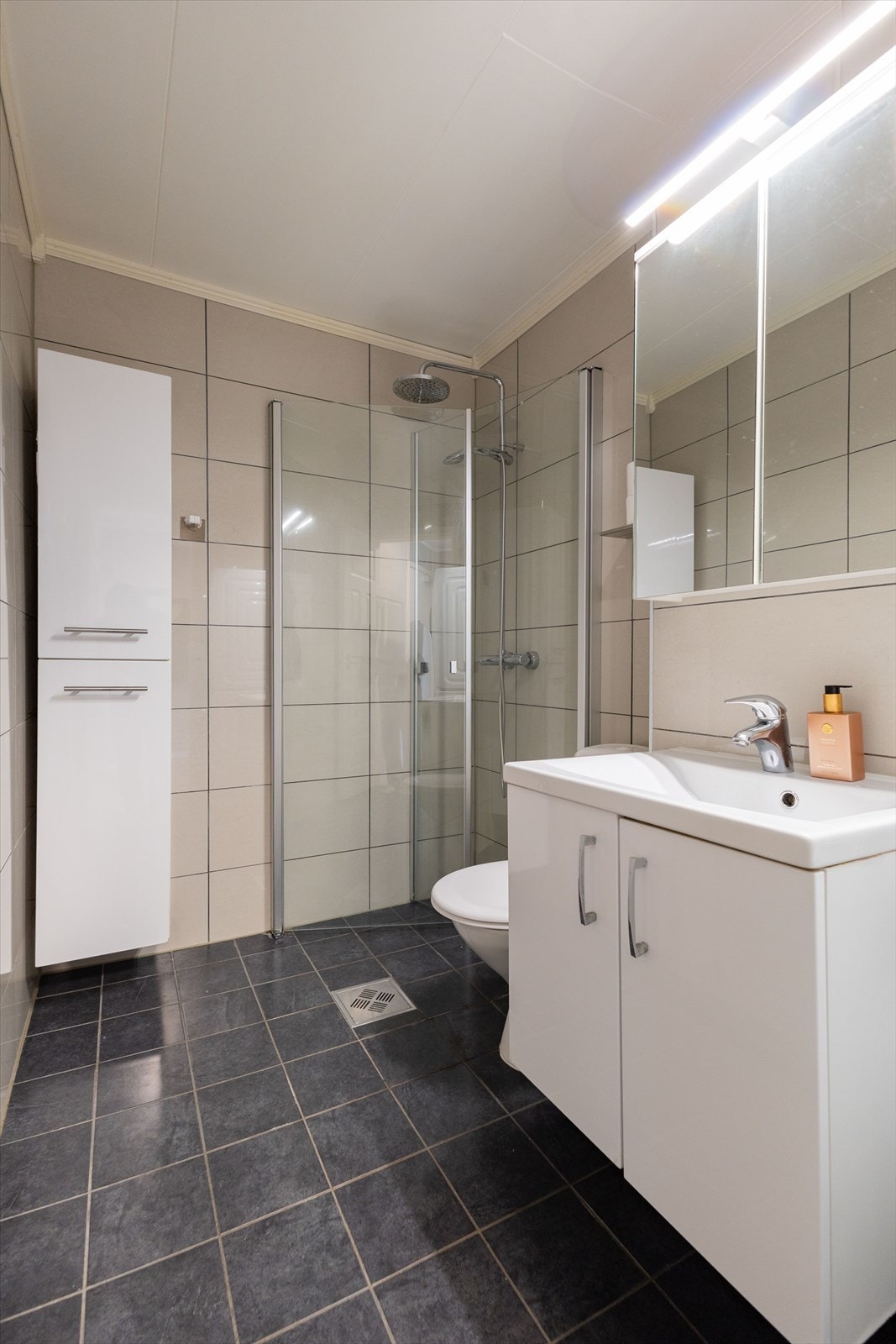 Bad utstyrt med opplegg for vaskemaskin, servantinnredning, WC på sokkel og dusjhjørne med glassdører. Galleribilde