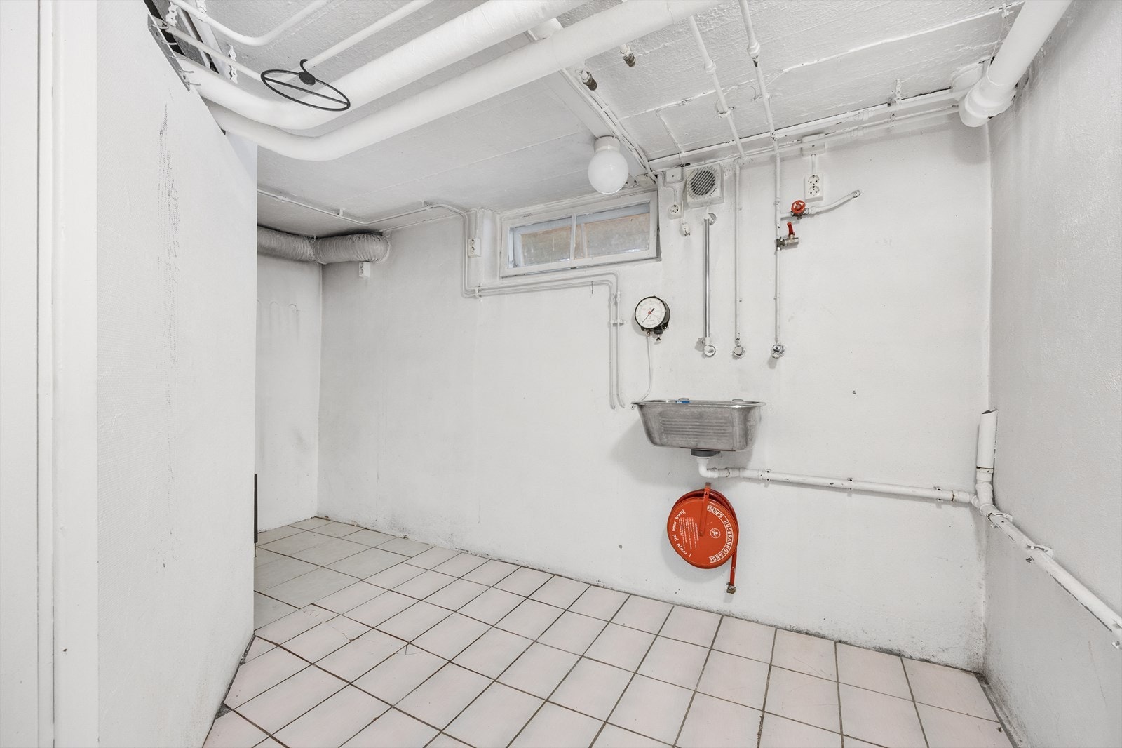 Praktisk vaskerom med flislagt gulv, utslagsvask og opplegg til vaskemaskin/tørketrommel. Galleribilde