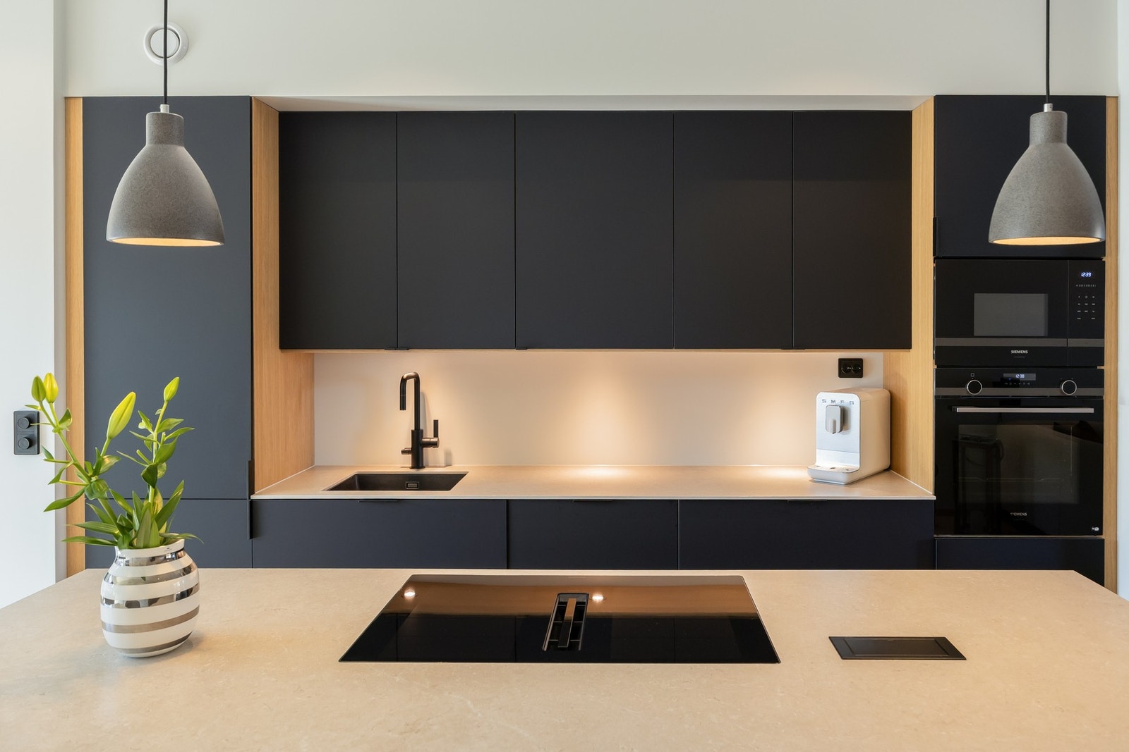 Robust og stilren benkeplate i stein med sømløs induksjonstopp med integrert avtrekksvifte. Øvrig integrerte hvitevarer som vinskap, mikrobølgeovn, stekeovn, og kombinert kjøle- og fryseskap. Galleribilde