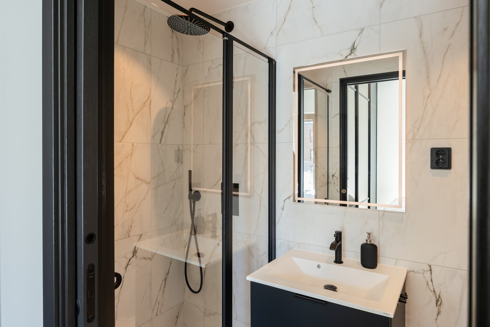 Stilfullt bad med direkte tilgang fra hovedsoverom, med smakfull utførelse med marmorflis og sorte detaljer. Galleribilde