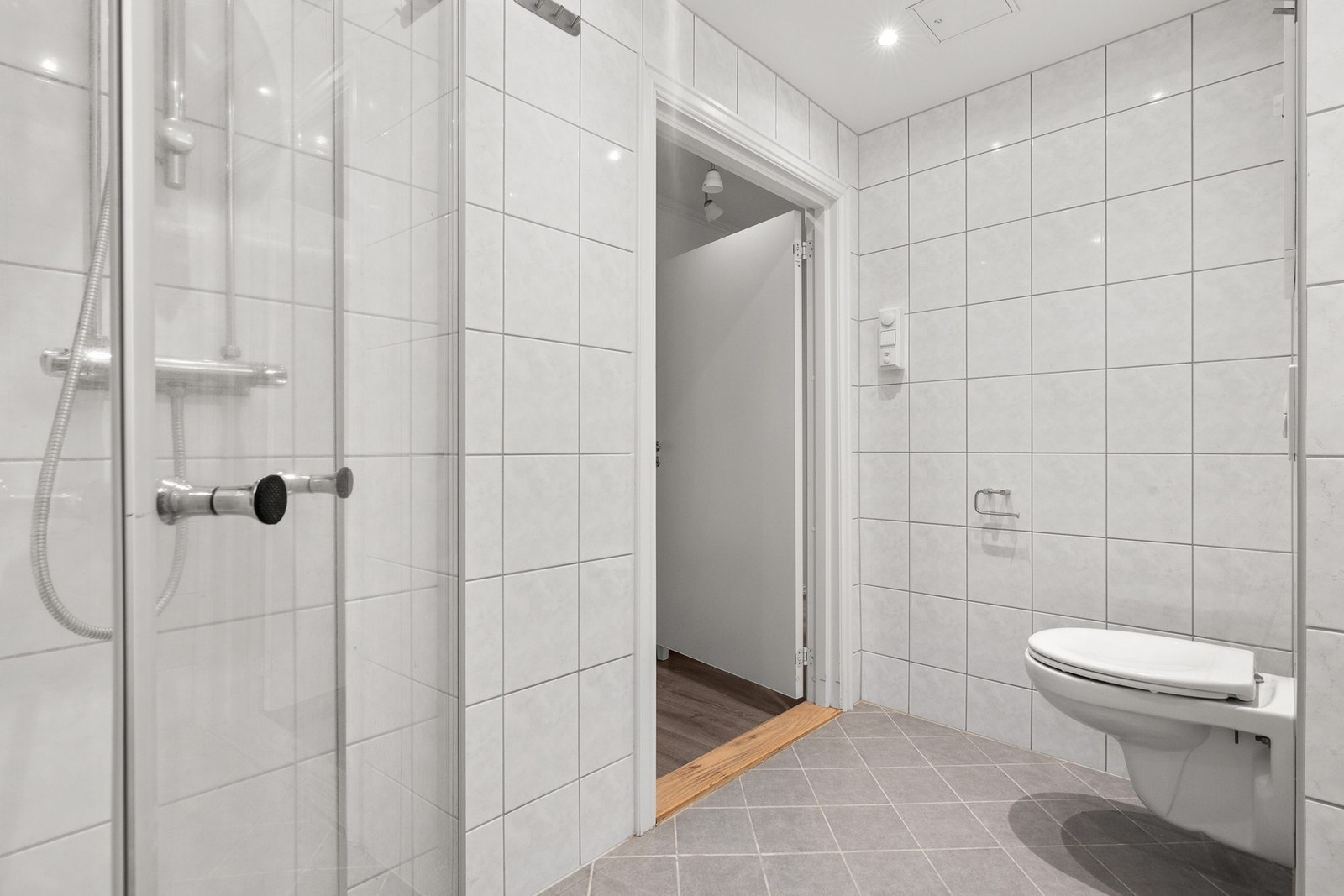 Badet inneholder vegghengt toalett, servantseksjon med skuffer, dusjhjørne med glassdører og opplegg for vaskemaskin. Galleribilde