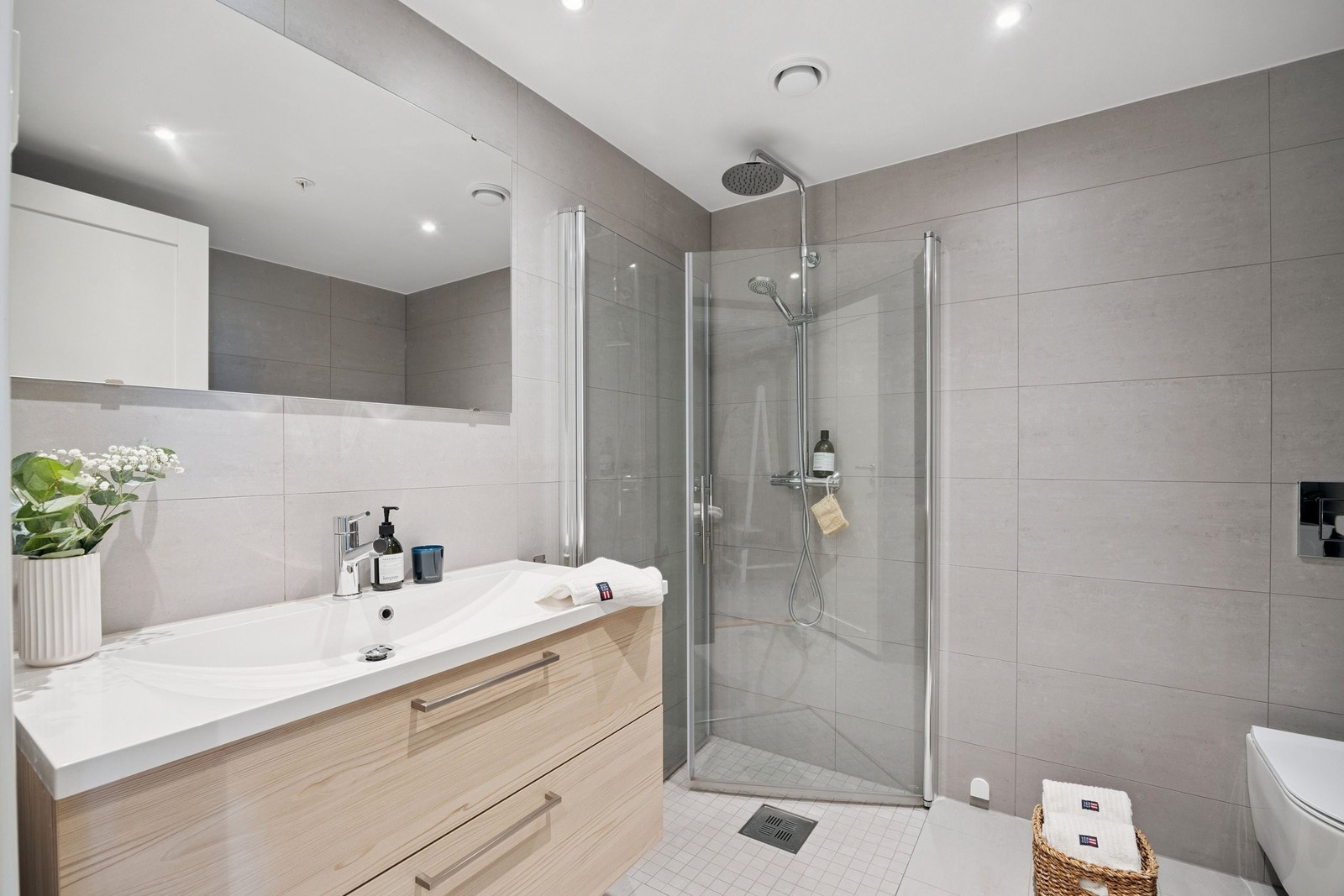 Lekkert baderom med store, lyse fliser på vegger og gulv, som gir et stilrent uttrykk. Galleribilde