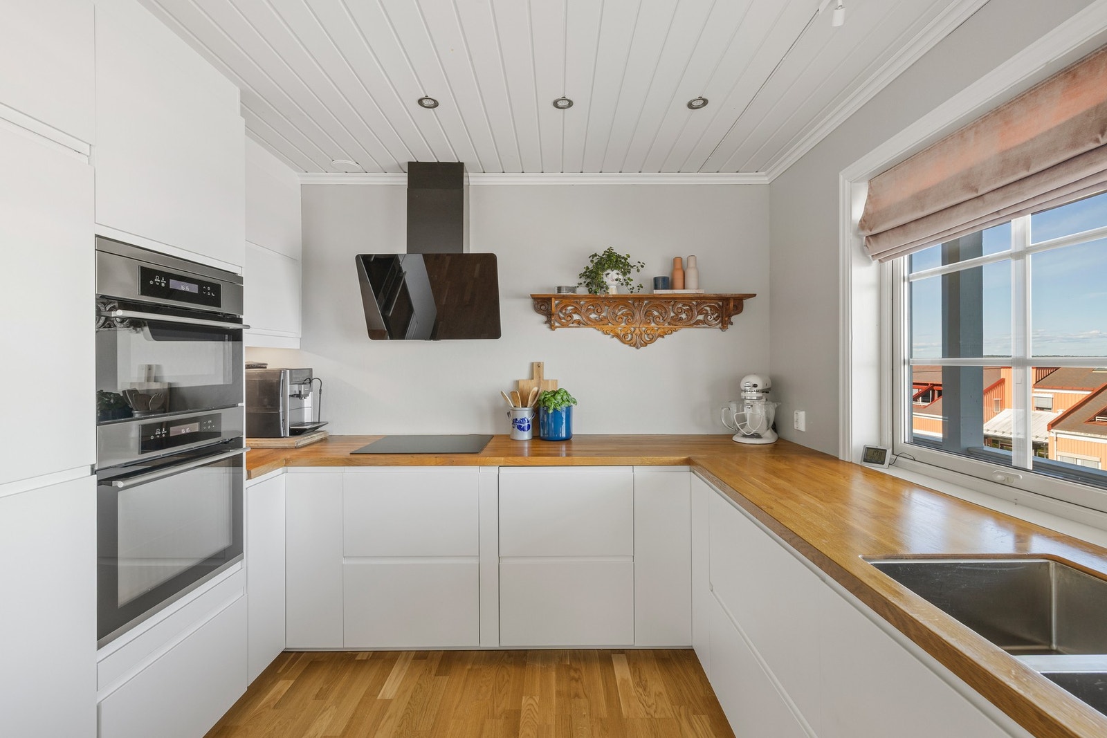 Innredningen har hvite, glatte fronter, takhøye skap og gyllen, solid benkeplate i heltre med underlimt kum i stål. Galleribilde