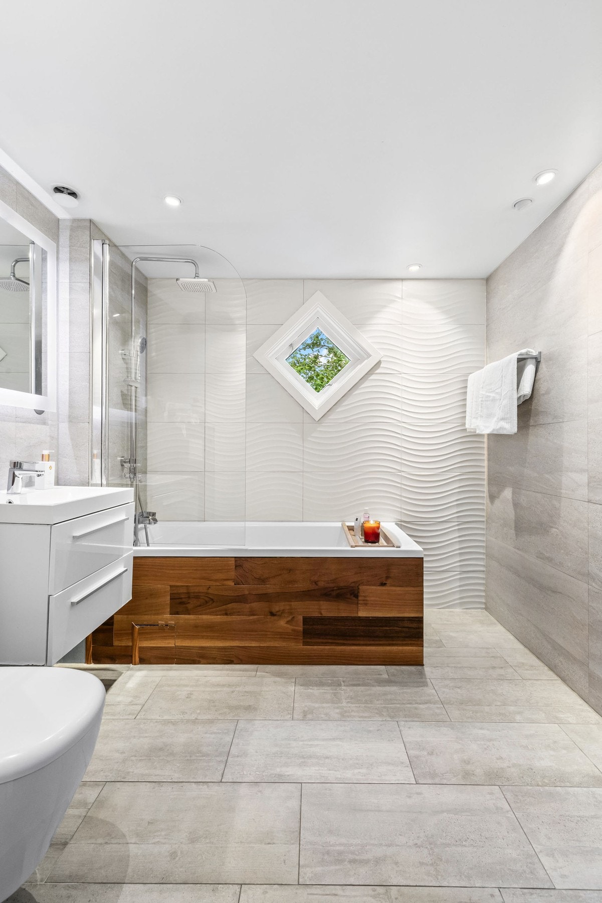 Delikat flislagt bad med downligts, gulvvarme og opplegg for vaskemaskin samt badekar med halv glassvegg og regnfallsdusj Galleribilde