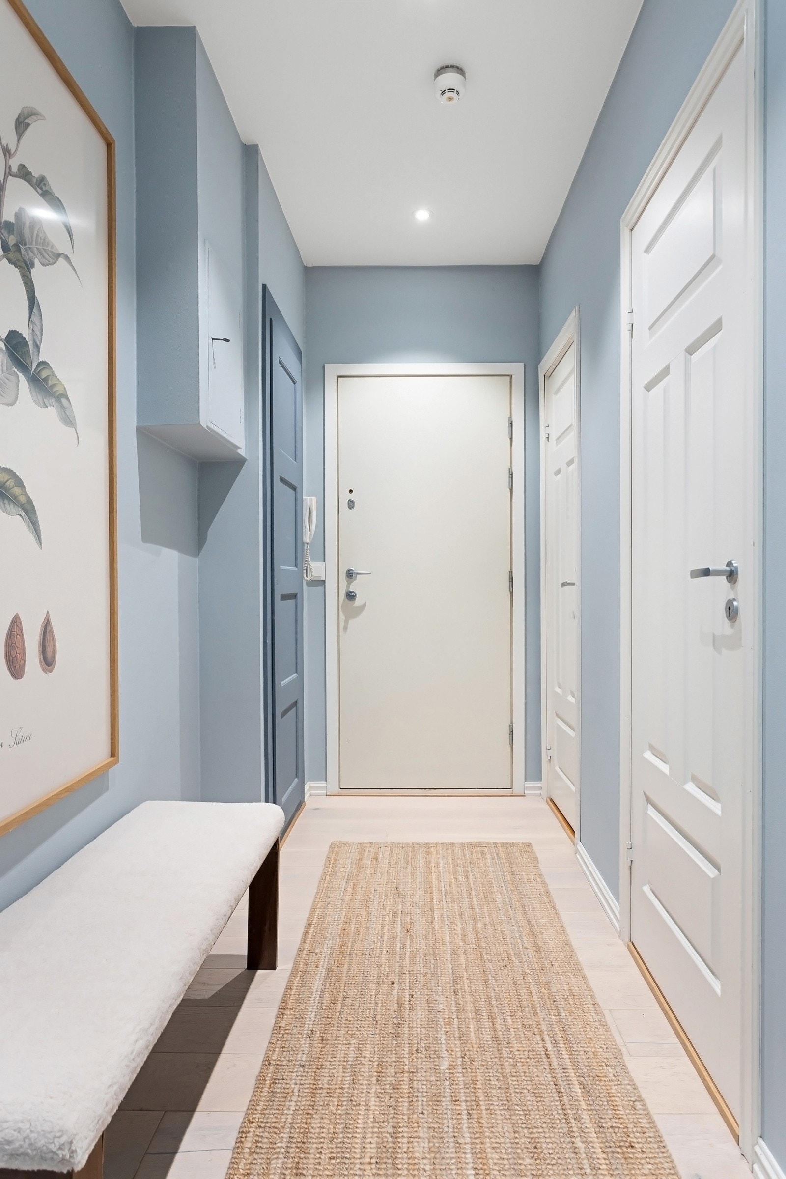 Entréen er innbydende og lys med vegger malt i en delikat, himmelblå nyanse, kombinert med hvitmalt himling og hvitpigmentert, enstavs parkettgulv. Galleribilde