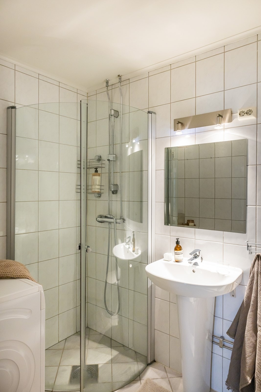 Lyst bad med flislagte overflater og varmekabler i gulv. Opplegg for vaskemaskin på badet. Galleribilde