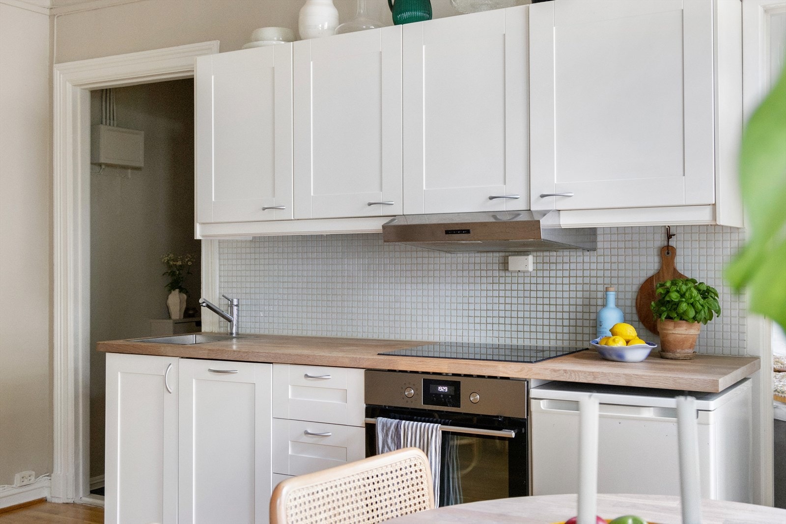 Kjøkkeninnredning med profilerte fronter og mosaikkfliser på vegg over benkeskap og belysning under overskap. Galleribilde