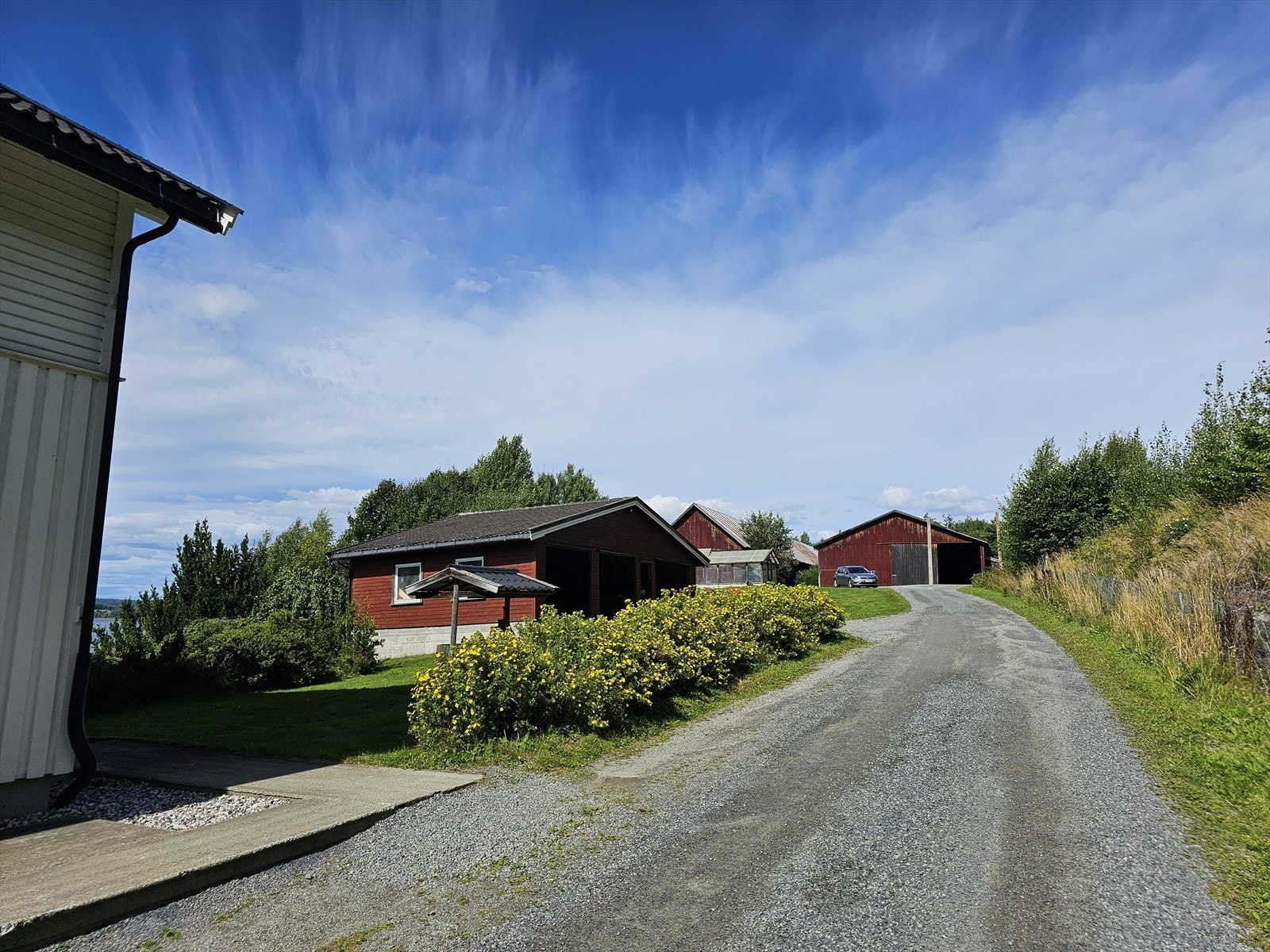Eiendommen gir et godt førsteinntrykk med gruset adkomstvei og gårdsplass som leder til garasjen med parkering for tre biler. Galleribilde